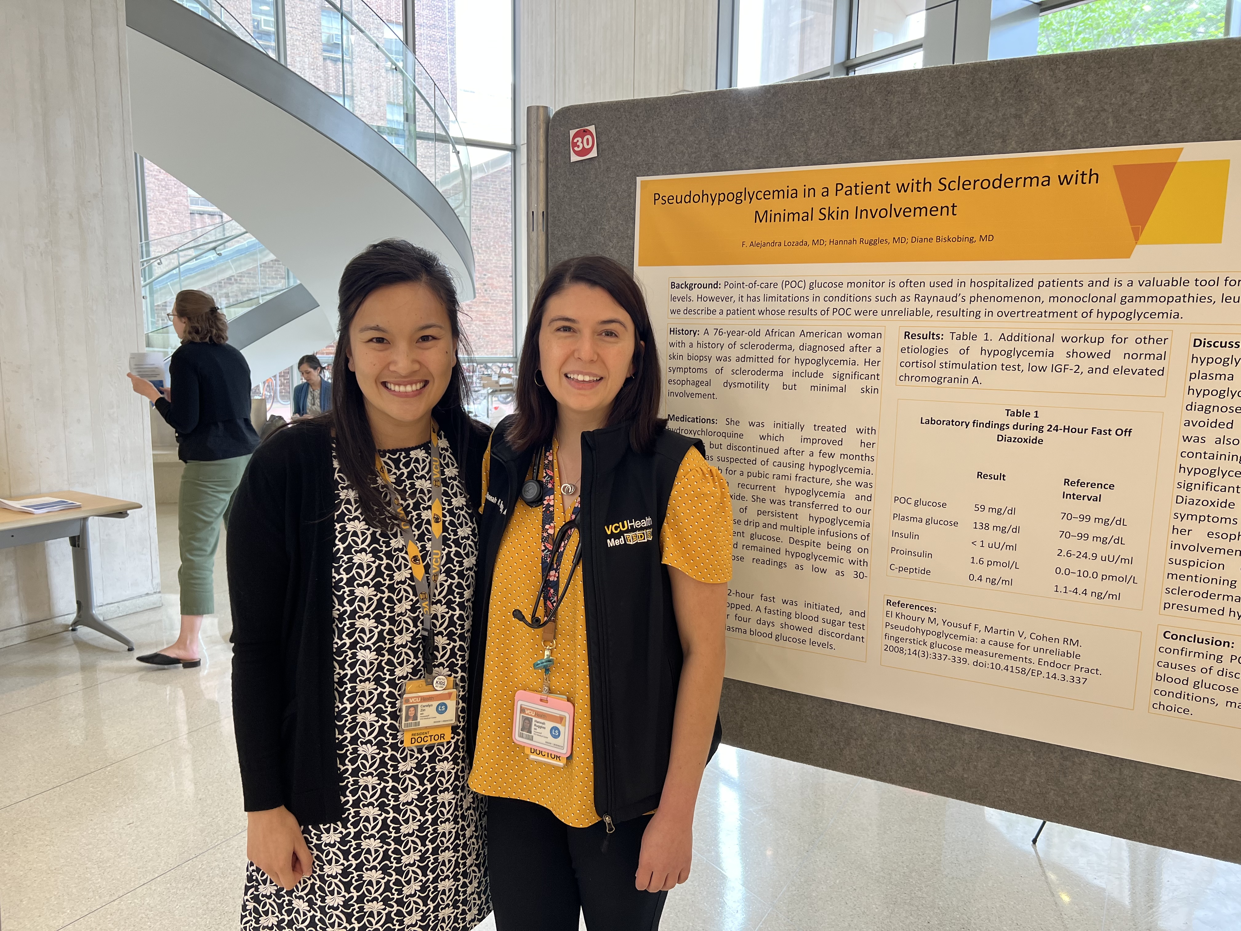 med-peds chiefs Drs. Carolyn Zin and Hannah Ruggles stand in front of a poster at GME Resident and Fellow Research Day